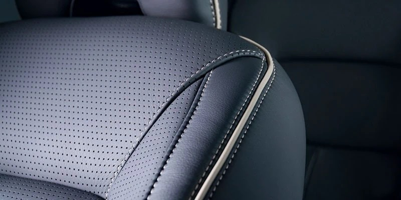 Close-up of dark perforated automotive upholstery, a smooth stitched bolster and pale piping